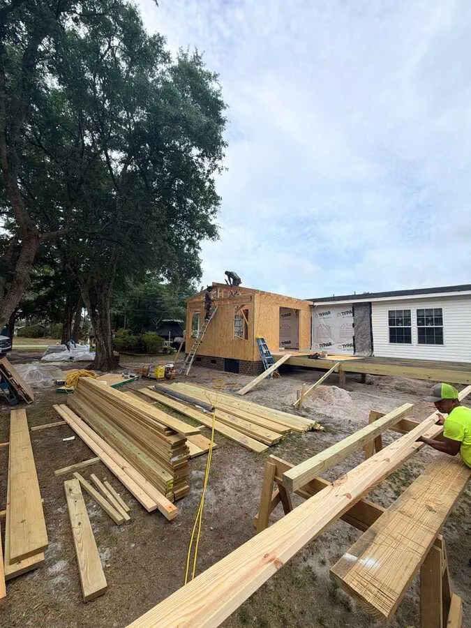 Lumber staged in front of a framed and sheathed home addition